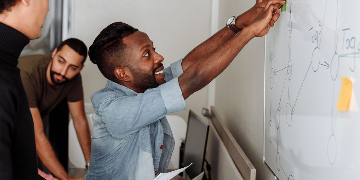A diverse product team actively brainstorming and collaborating on solutions at a whiteboard.